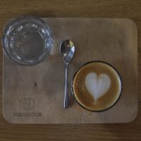 A flat white, made with a San Rafael from Honduras, one of two daily single-origins on espresso at Dos Mundos in Prague. Served in a glass, it's presented on a wooden tray with a glass of water on the side.