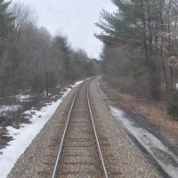 The view from the final carriage of Amtrak's Adirondack service on its way from New York City to Montréal in March 2013, looking back over the single track as it passes through woods north of Albany.
