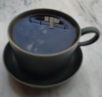 A cup of filter coffee on the window-bar of Potter & Reid, with the sky reflected in the surface of the coffee.